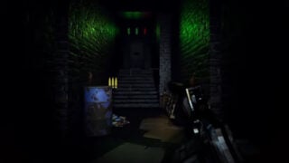 screenshot from the paracam trailer with a POV of the player holding a gun while walking toward a set of stairs that leads to a dark door, there are two green lights above the door as well as a red one, as a metal barrel stands at the bottom of the stairs amongst some rubbish on the ground